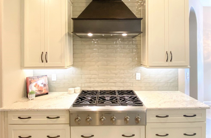 white cabinets with stone countertops and custom tile backsplash with oven hood vent